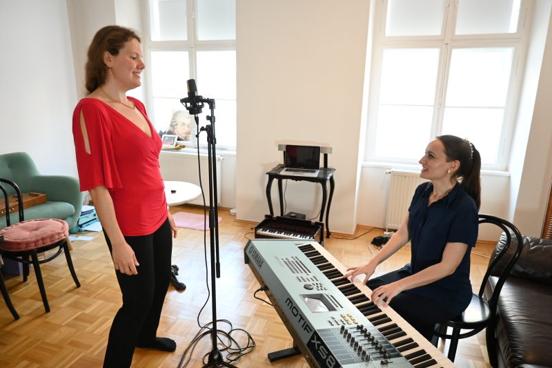 Gesangsunterricht: Links steht die Schülerin und singt in ein Mikrofon. Rechts sitzt Elisabeth Schulz, spielt Synthesizer und lächelt.