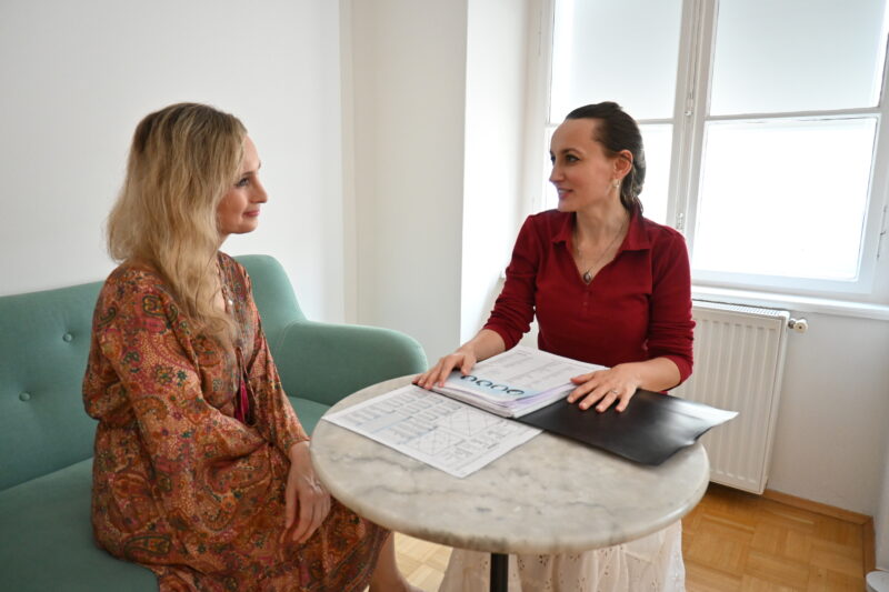 Vedische Astrologie Beratung von Elisabeth Schulz mit einer Kundin. Beide sitzen an einem Tische. Elisabeth sitzt am Sessel und die Kundin sitzt am türkisen Sofa