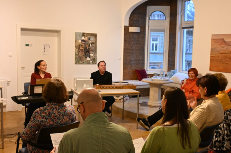 Elisabeth Schulz spielt Keaboard und Emanuel Schulz sitzt vor einer indischen Harfe. Die Teilnehmer sitzen gegenüber und hören zu. Dies ist ein Seminar mit indischer Musiktherapie, die live gespielt und gesungen wird.